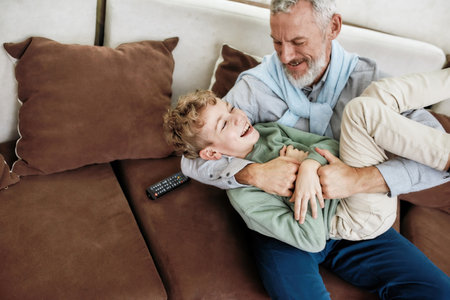 Best friends. Portrait of cheerful grandfather and excited grandson embracing, playing and having fun while relaxing on a couch at homeの写真素材