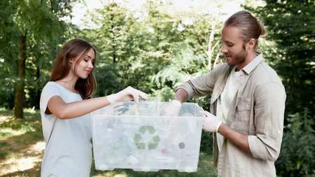 Young beautiful couple holding recycle bin, collecting plastic waste in the forest or park