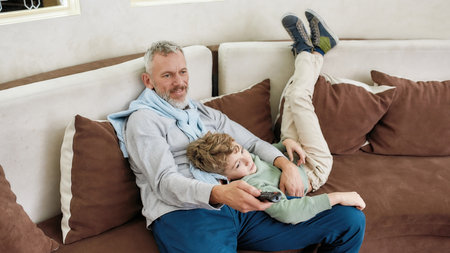 Family time. Portrait of a happy grandfather and excited grandson embracing, having fun and playing while relaxing on a couch at homeの写真素材