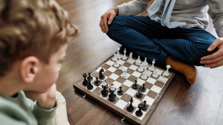 Intellectual game. Little thoughtful boy playing chess with grandfather while sitting on the floor in living room at homeの写真素材