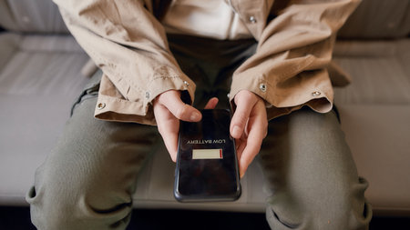 Close up of female hands holding mobile phone while sitting on back seat in the car. Low battery notification on the screenの写真素材