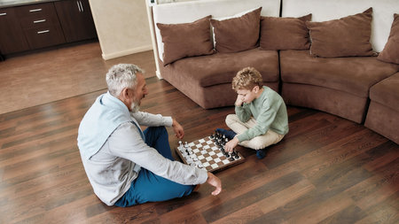 Grandpa teaching his grandson best chess strategy and tactics while sitting together on the floor in the living room, spending time at homeの写真素材