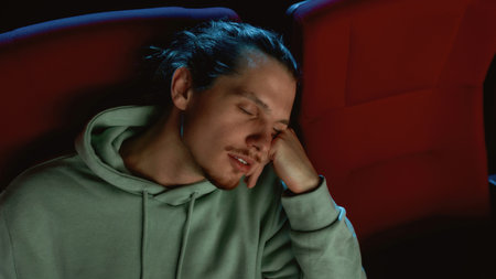 Portrait of young man falling asleep in chair while watching a movie at the cinemaの写真素材