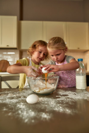 Little cooks. Adorable little children, boy and girl in aprons looking focused while preparing dough together on the kitchen table at homeの写真素材