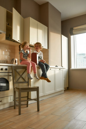 Portrait of two joyful kids, brother and sister eating cornflakes while sitting together on the kitchen cabinet at homeの写真素材