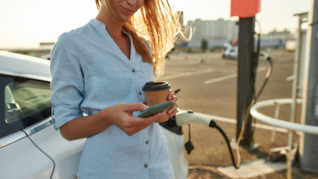 Woman scrolling phone while waiting for car chargingの写真素材