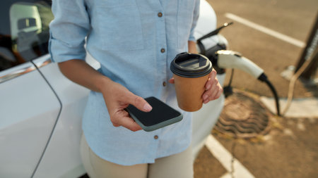 Smartphone in hands of girl waiting for vehicle chargingの写真素材