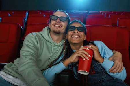 Portrait of happy young couple wearing 3d glasses smiling while watching a comedy together in cinema auditorium and drinking sodaの写真素材