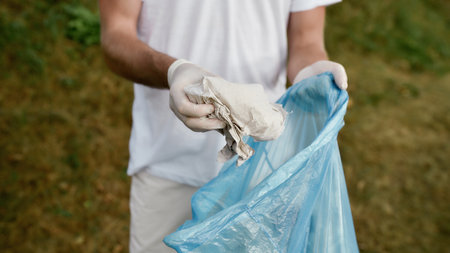Young male volunteer wearing uniform and rubber gloves collecting trash and garbage in the forest or...