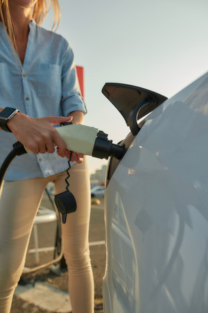 Woman plugging electricity cable in vehicle for chargingの写真素材