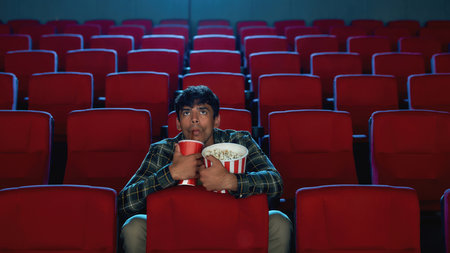 Focused handsome young man holding a drink and popcorn basket while watching movie alone in empty theater auditoriumの写真素材