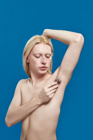 Young caucasian man shaving armpit using razorの写真素材