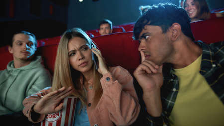 Portrait of attractive young woman talking on the phone, annoying her boyfriend while having romantic movie date at the cinemaの写真素材