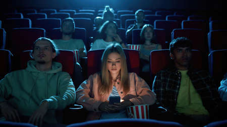 Beautiful young woman using her phone for texting while watching a movie at the cinema