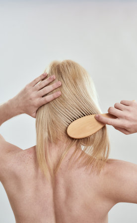 Young shirtless man grooming his long blond hairの写真素材