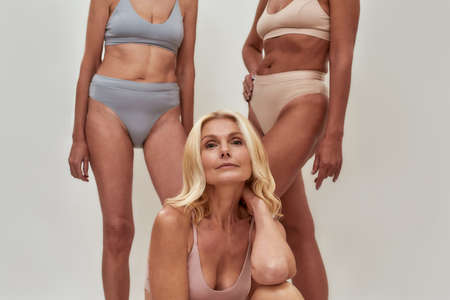 Beautiful blonde caucasian senior woman in underwear looking at camera while posing together with...
