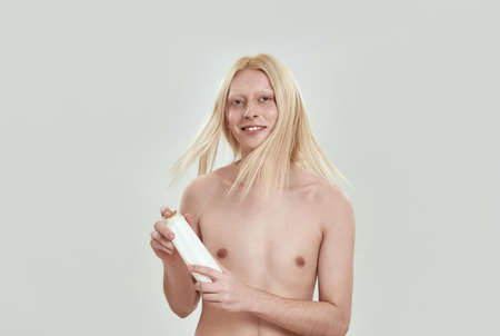 Model shaking head with blond hair while holding shampooの写真素材