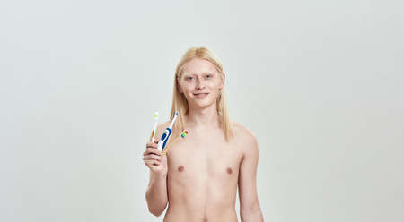 Young caucasian blond man holding different toothbrushes in handの写真素材