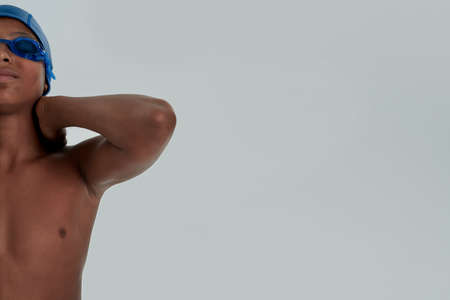 Young people and sport. Half face portrait of a teenage african boy in swimming cap and goggles keeping arms on his neckの写真素材