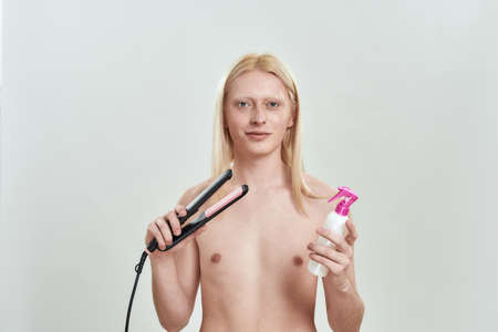 Young caucasian man holding hair straightener and fixation foamの写真素材