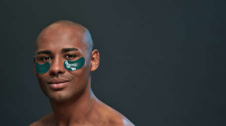 Male smirking while keeping green cosmetic patches under eyes