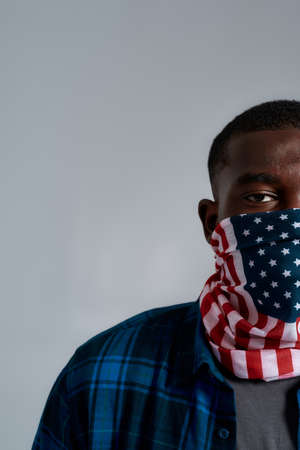 Half face portrait of young african american male protester, activist wearing bandana mask with american flag print while posing isolated over gray backgroundの写真素材
