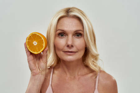 Kind woman raising an orange to her faceの写真素材