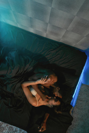 Top view of a young beautiful smiling mixed race couple lying on the bed, kissing and hugging,...