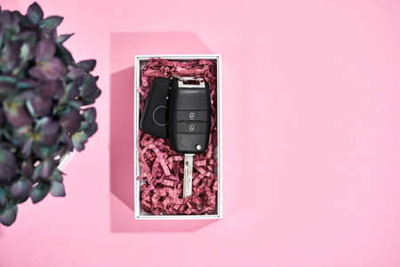 Surprise for her. Top view of a car key in present box and flowers on pastel pink backgroundの写真素材