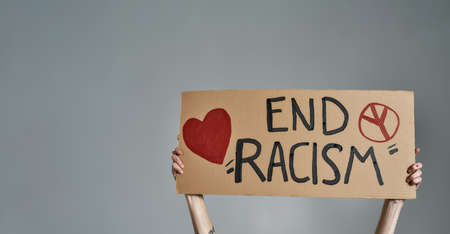 Close up shot of female hands holding cardboard banner with End Racism text isolated over gray backgroundの写真素材