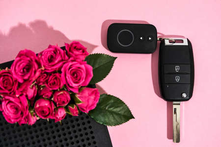 Surprise for her. Close up of little pink roses and black car key on pink background, flat layの写真素材