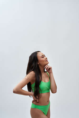 Studio shot of happy young woman wearing green underwear looking away, posing isolated over light backgroundの写真素材