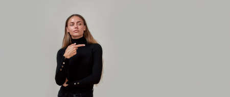 Elegant young caucasian woman dressed in black looking away and pointing at something on the right...