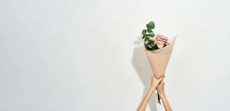 Happy Womens day. Female hands holding beautiful flowers bouquet wrapped in craft paper over light...
