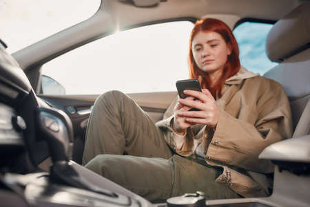 Portrait of teenage girl looking at the screen while using her phone, sitting in the car. Smartphone...