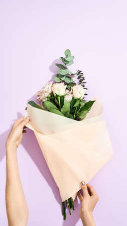 Female florist wrapping fresh flowers bouquet in craft paper on purple background, top viewの写真素材