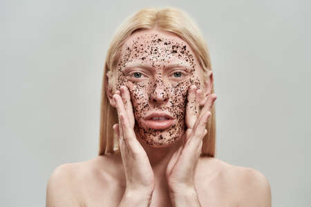 Portrait of young blond boy applying scrub on faceの写真素材