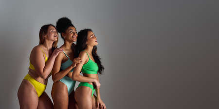 Three diverse young women with different body shapes wearing colorful underwear smiling aside, posing together isolated over grey backgroundの写真素材