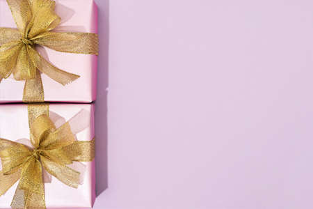 Top view of two small wrapped gift boxes with golden bows on pink background, copy space for textの写真素材