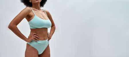 Cropped shot of curvy young woman wearing blue underwear posing for camera, standing isolated over light backgroundの写真素材