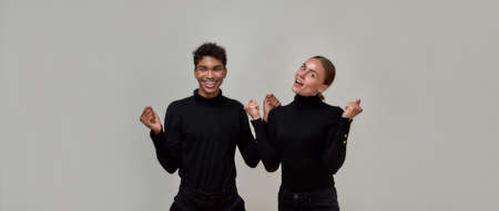 Excited young guy and woman dressed in black smiling at camera, doing a winner gesture together, standing isolated over gray backgroundの写真素材