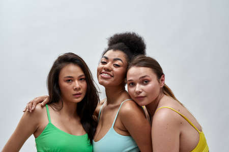 Studio portrait of three confident multiethnic women in colorful underwear posing together isolated...