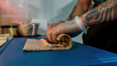 Close up of hands in protective gloves of sushi chef wrapping staff inside roll with bamboo matの写真素材