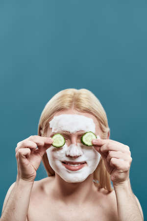 Man washing face with foam mask and cucumber slices