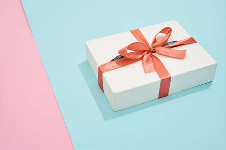 White gift box with red bow on pink and blue backgroundの写真素材
