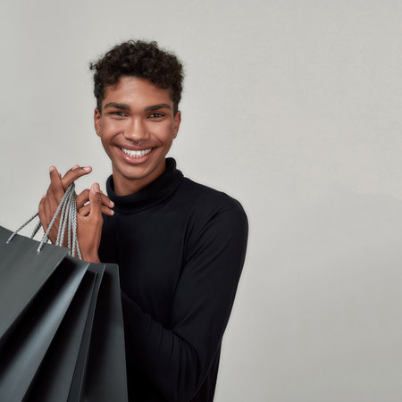 Portrait of smiling young man holding black paper bagsの写真素材