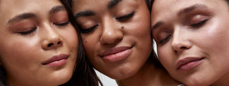 Cropped portrait of faces of three diverse women posing together with eyes closed over light backgroundの写真素材