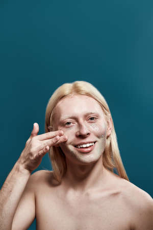 Young blond caucasian man applying cleansing maskの写真素材