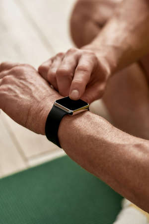 Cropped shot of a man using his smart watch while exercising, working out at homeの写真素材