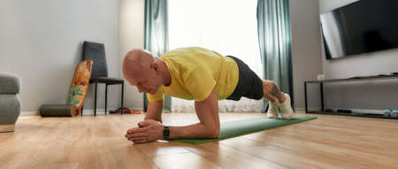 Time for fitness. Athletic mature man in sportswear standing in a plank on yoga mat while exercising...